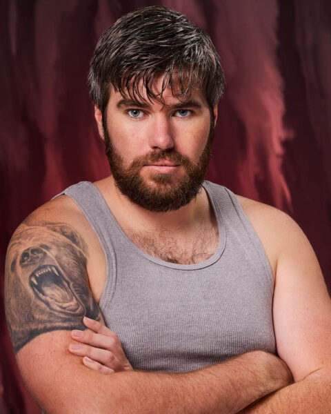 A theatrical actor headshot of a bearded man in a tank top in a studio near Los Angeles with a copper background
