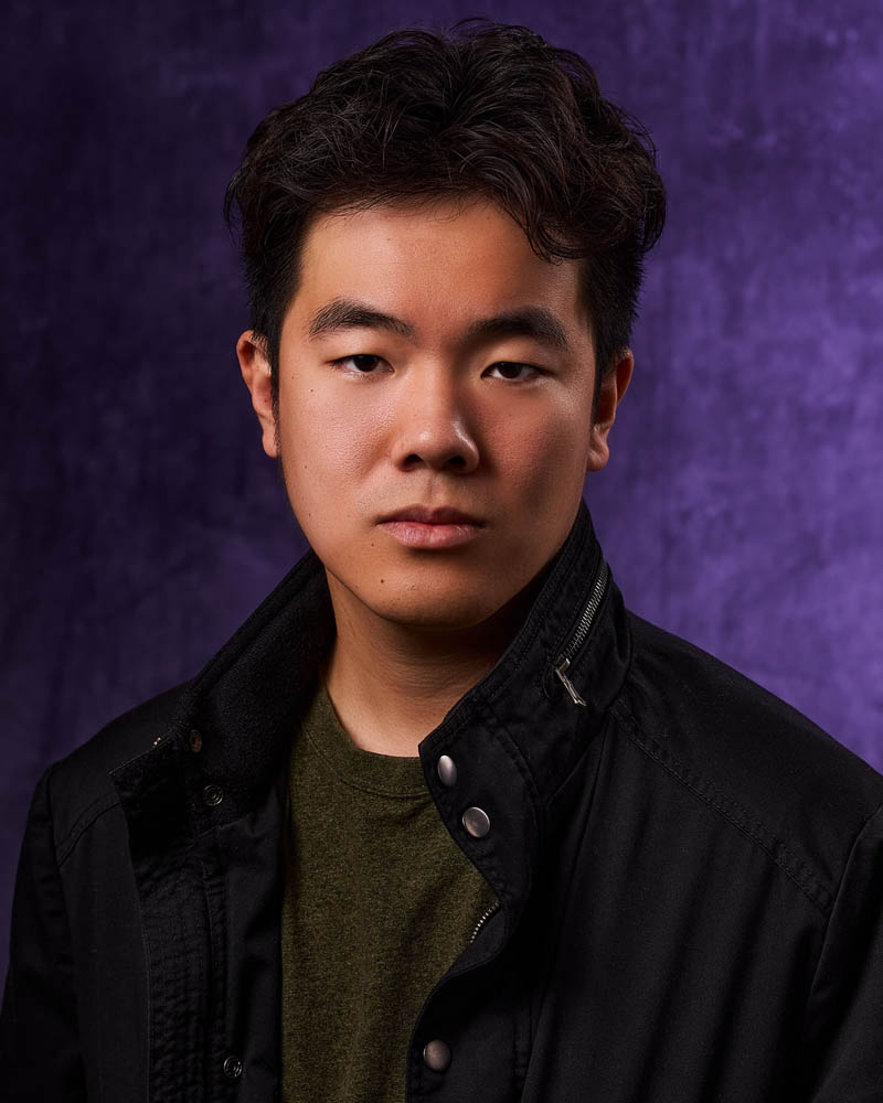 A theatrical actor headshot of an Asian man in a jacket in a studio near Pasadena with a purple background