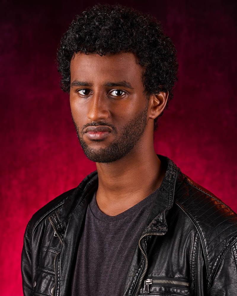 A theatrical actor headshot of a dramatic man in leather in a studio near Los Angeles with a red background