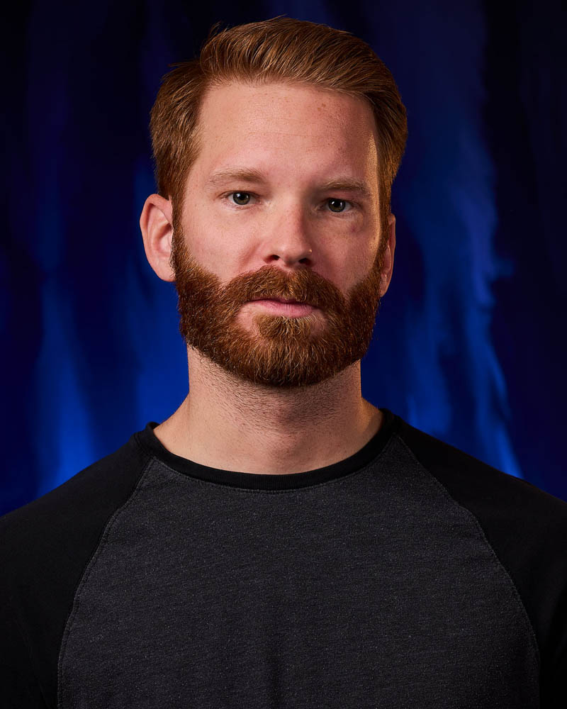 A dramatic actor headshot of a man with a beard in a studio near North Hollywood with a blue background