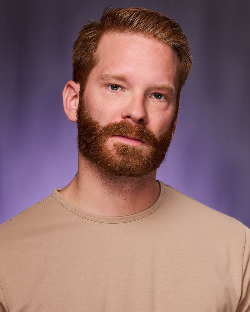 A theatrical actor headshot of a man with a beard n a studio near North Hollywood with a purple background