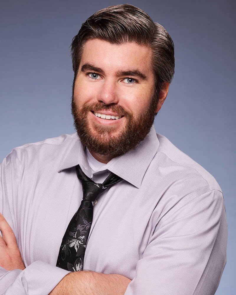 A commercial actor headshot of a bearded man in a tie in a studio near Burbank with a blue background