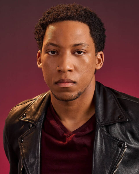 A theatrical actor headshot of a black man and leather jacket in a studio near Pasadena with a red background